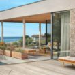 Façade de maison en parement Tertus à côté d'une terrasse en bois et d'une piscine creusée, à proximité d'une plage.